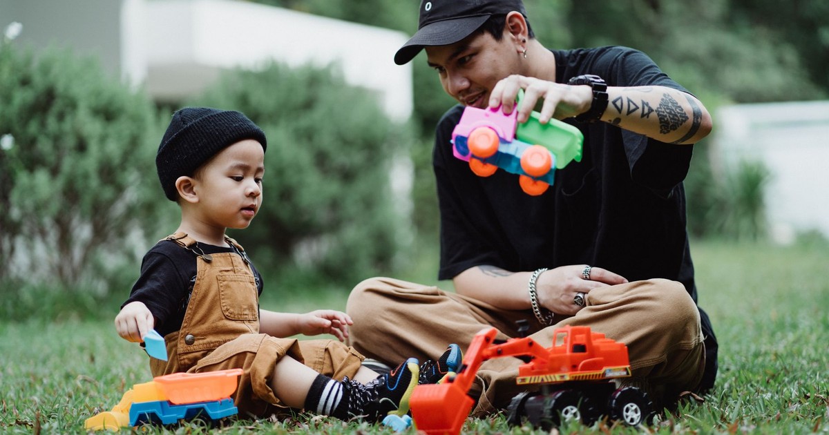 Father and son bonding over toy trucks on a grassy yard. Capturing moments of play and parenting.