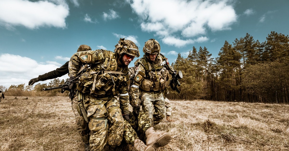 Military personnel actively engaged in outdoor rescue operation on grassy field, showcasing teamwork and bravery.