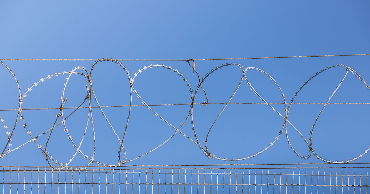Detailed image of barbed wire fence under clear blue sky, symbolizing security and restriction.