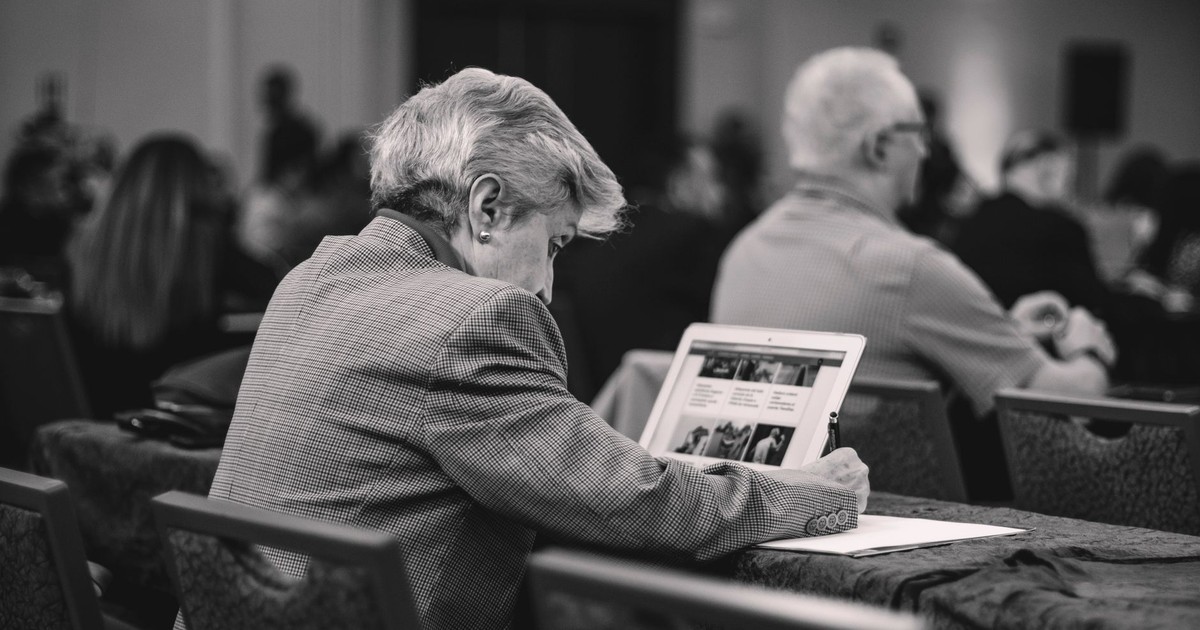 A senior journalist takes notes during a conference, engrossed in thought.