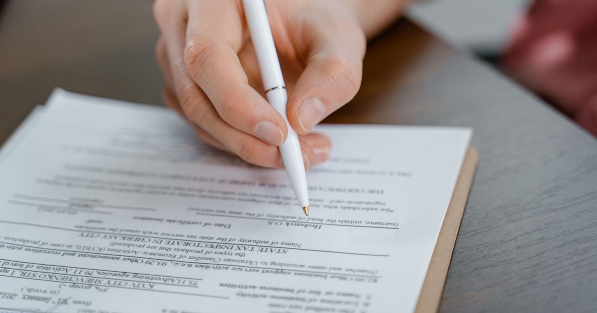 A hand holding a pen signing a document, close-up shot with focus on the paper.