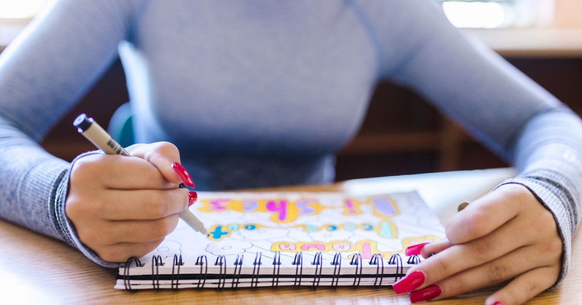 Woman drawing in a notebook with colorful pens in an indoor setting, showcasing creativity and focus.