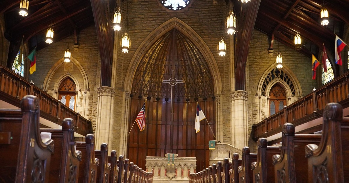 Interior view of a gothic-style church with wooden arches, flags, and ambient lighting.