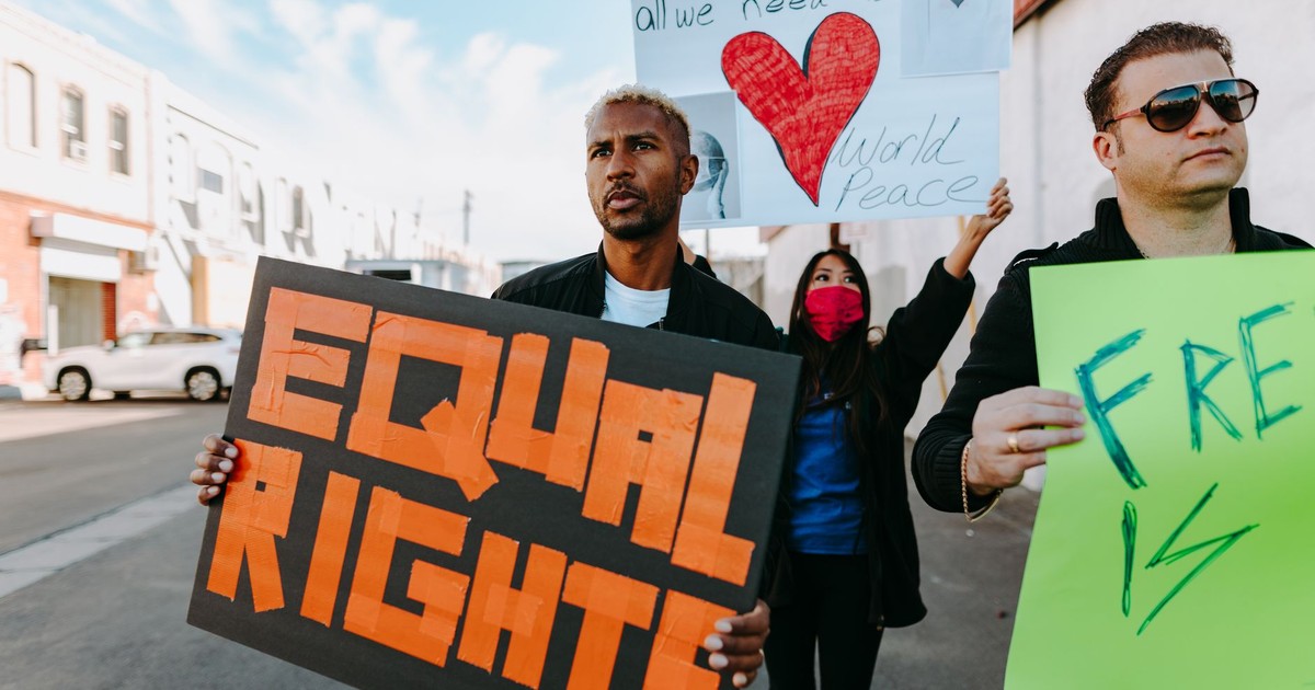 A diverse group of protesters holding signs advocating for equal rights and world peace.