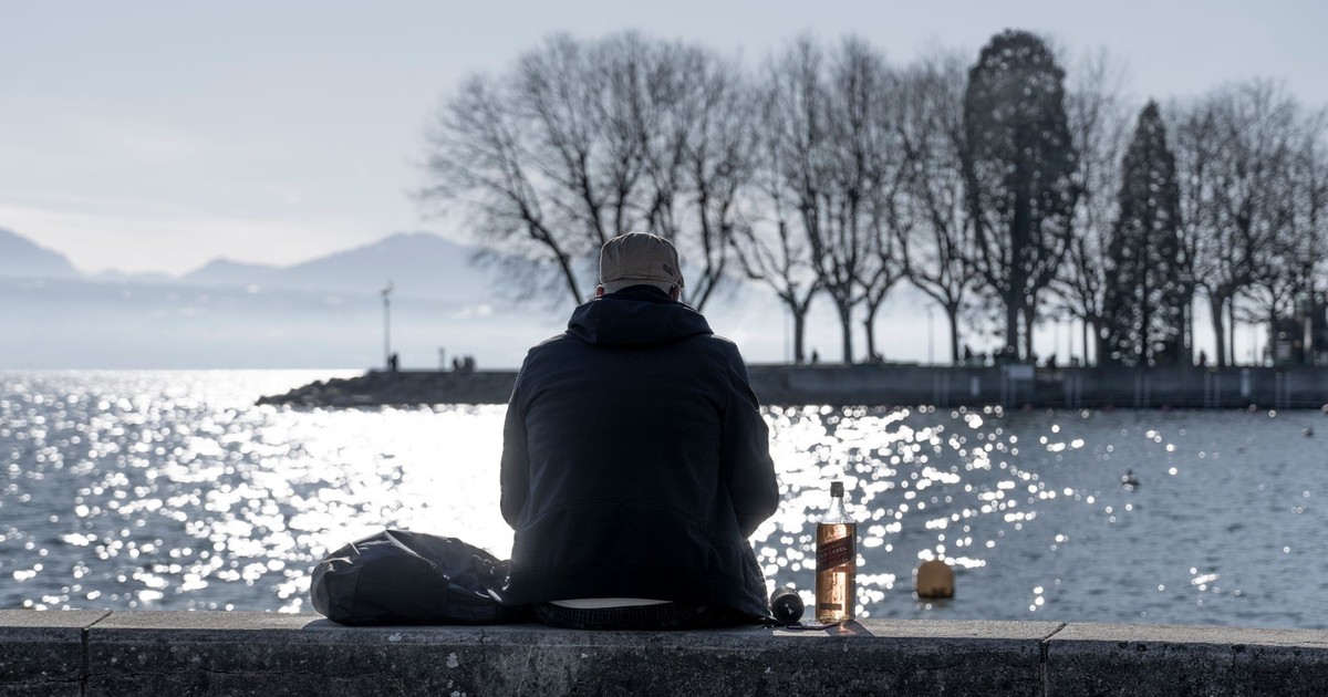 A solitary man in a jacket facing a body of water in a park, reflecting on life.