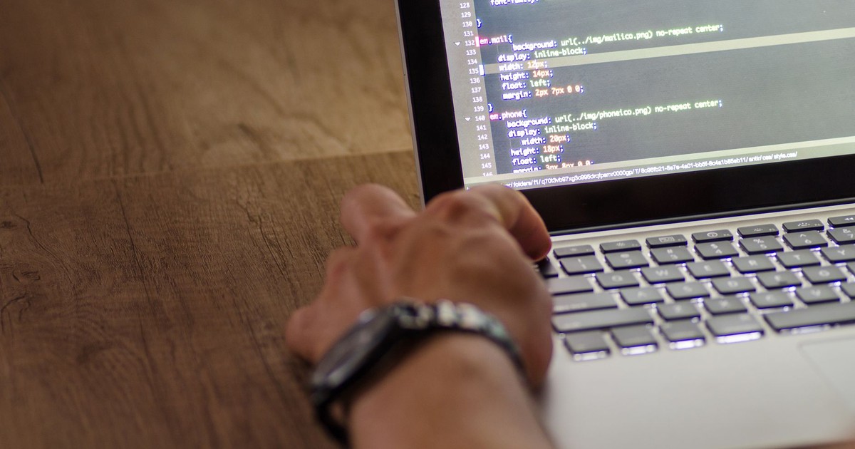 A developer's hand interacting with code on a laptop screen in a workspace setting.