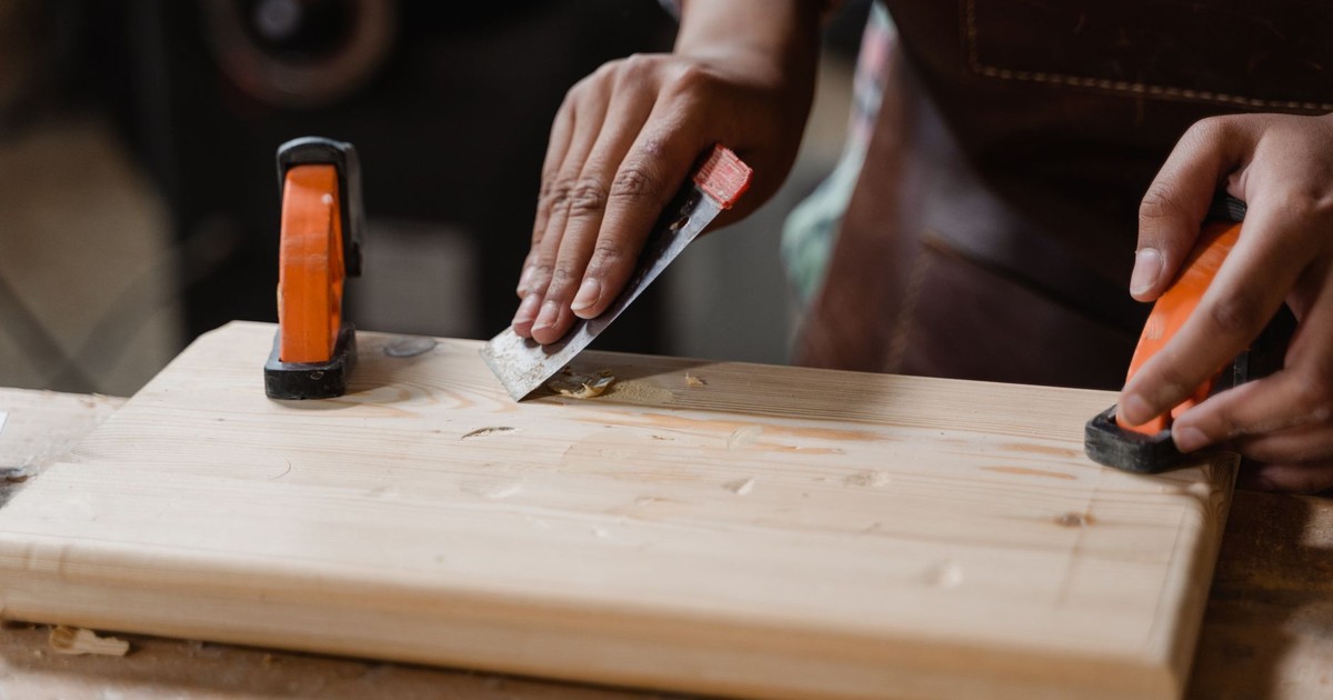 Hands crafting a wooden plank with clamps and tools. A focus on precision woodworking.