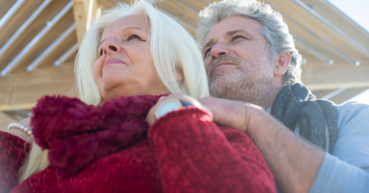 Loving senior couple embracing outdoors, under wooden structure in sunny Portugal.
