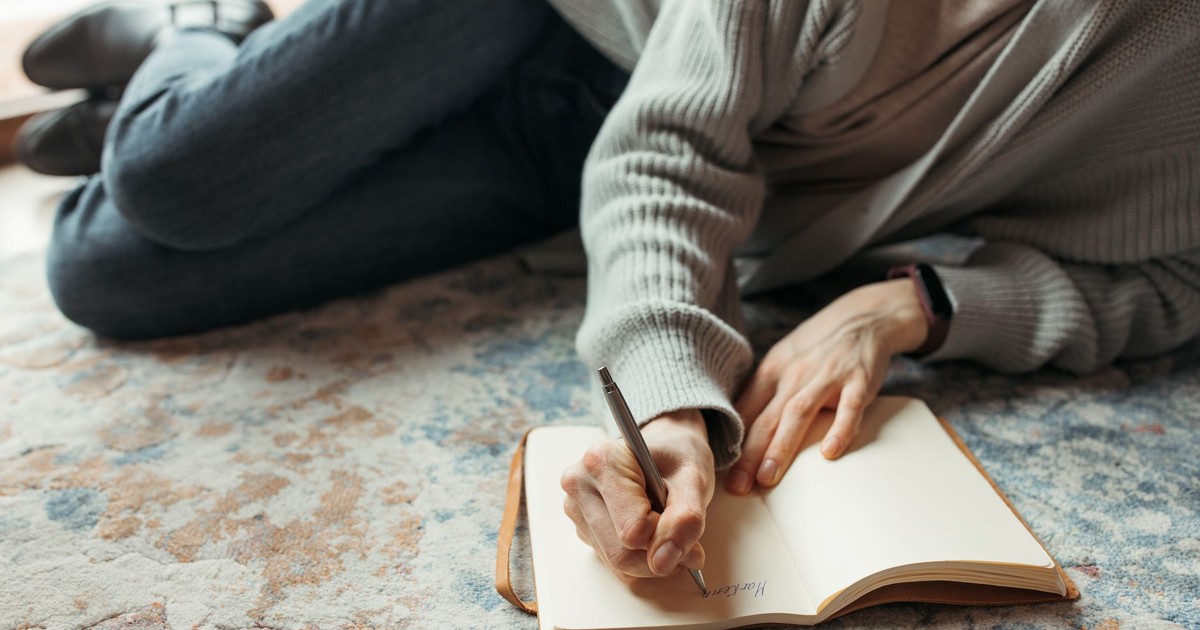 A person lies comfortably on the floor, writing in a journal with a pen, symbolizing creativity and relaxation.