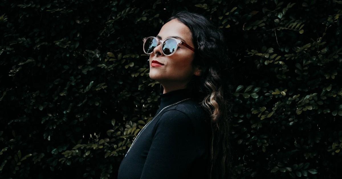 Fashionable woman with sunglasses posing outdoors in São Paulo, Brazil against a leafy background.