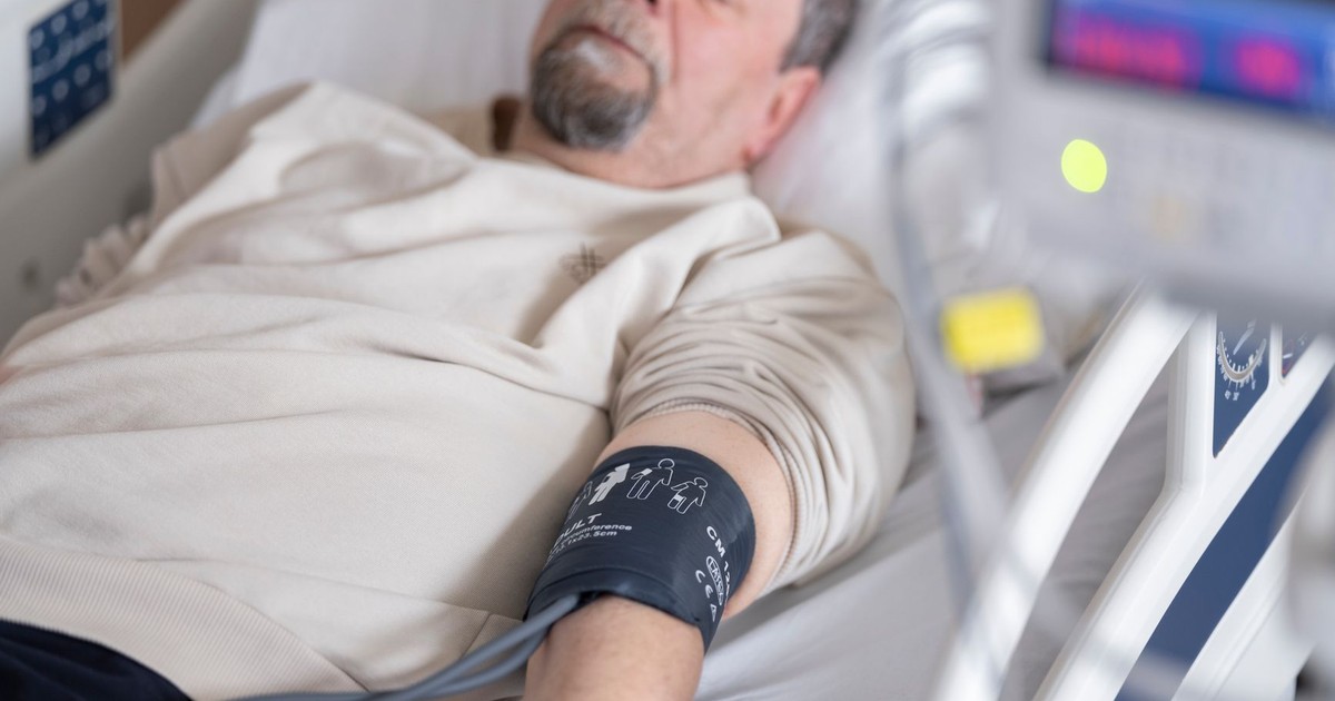 Elderly man resting in hospital bed with blood pressure monitor attached, symbolizing healthcare and medical care.