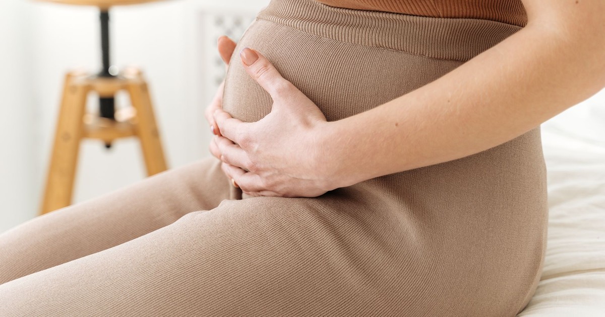 A serene close-up of a pregnant woman gently holding her belly, captured in soft natural light.