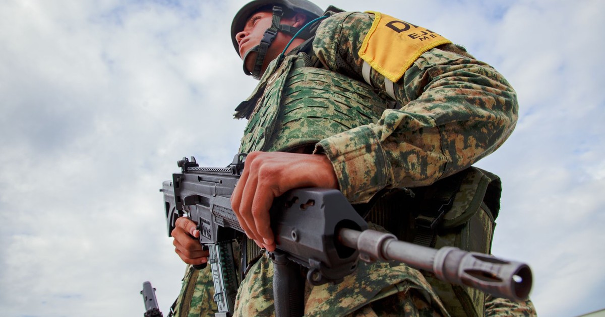 Close-up of a soldier in camouflage holding a rifle under a blue sky, representing military readiness in Mexico.