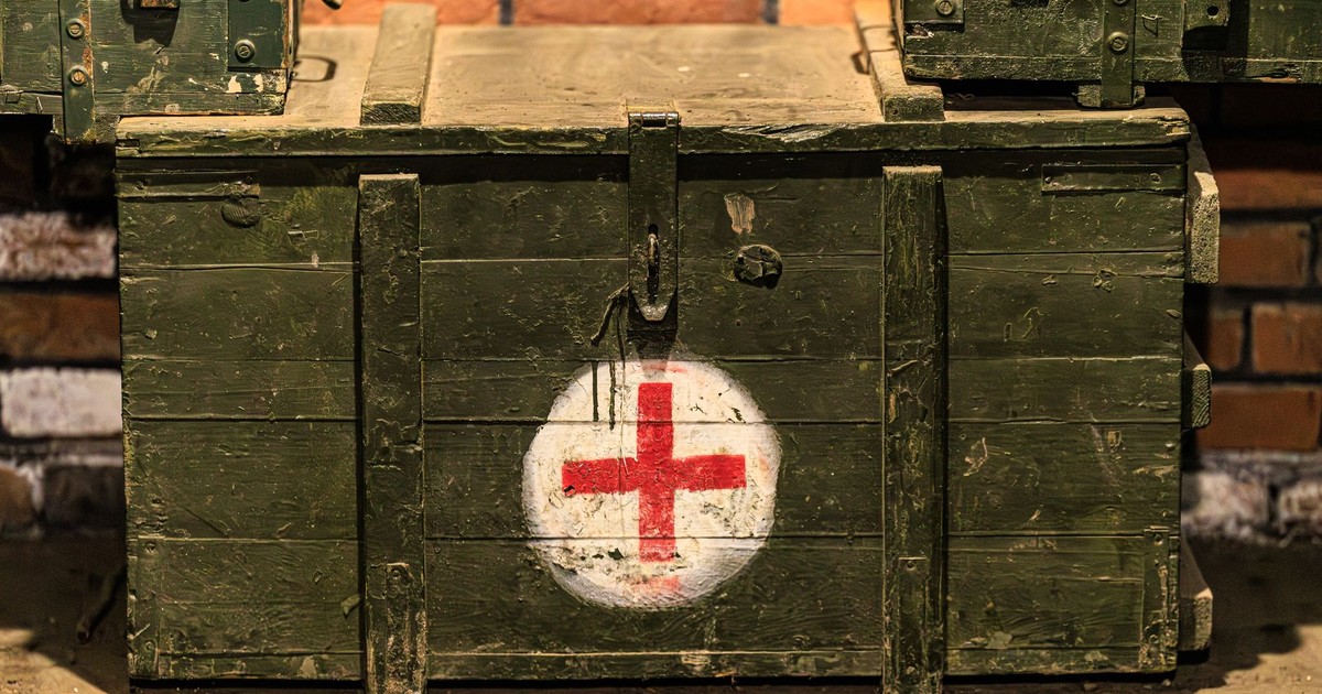 Close-up of a vintage military medical crate with a red cross, set against a rustic brick wall.