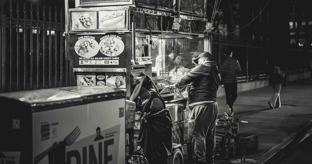 Black and white photo of a food vendor in New York City, capturing urban night life.