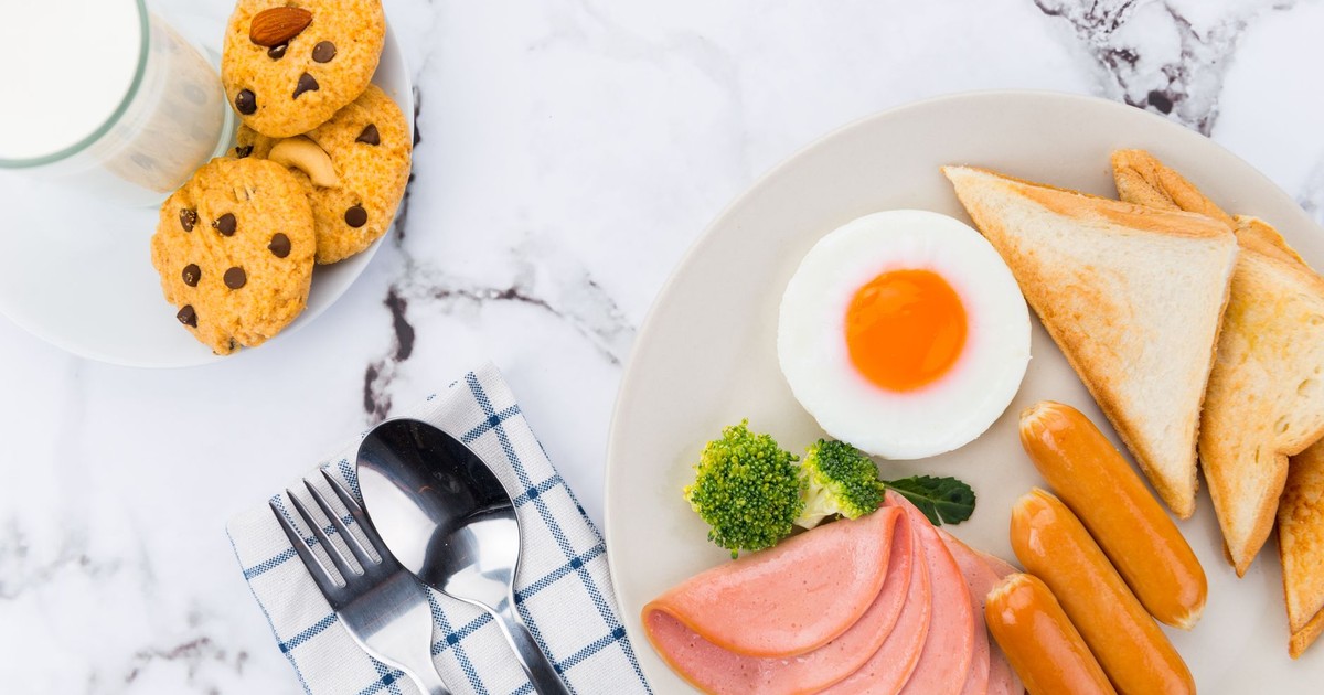 A close-up of a breakfast platter with egg, sausages, ham, toast, cookies, and milk.
