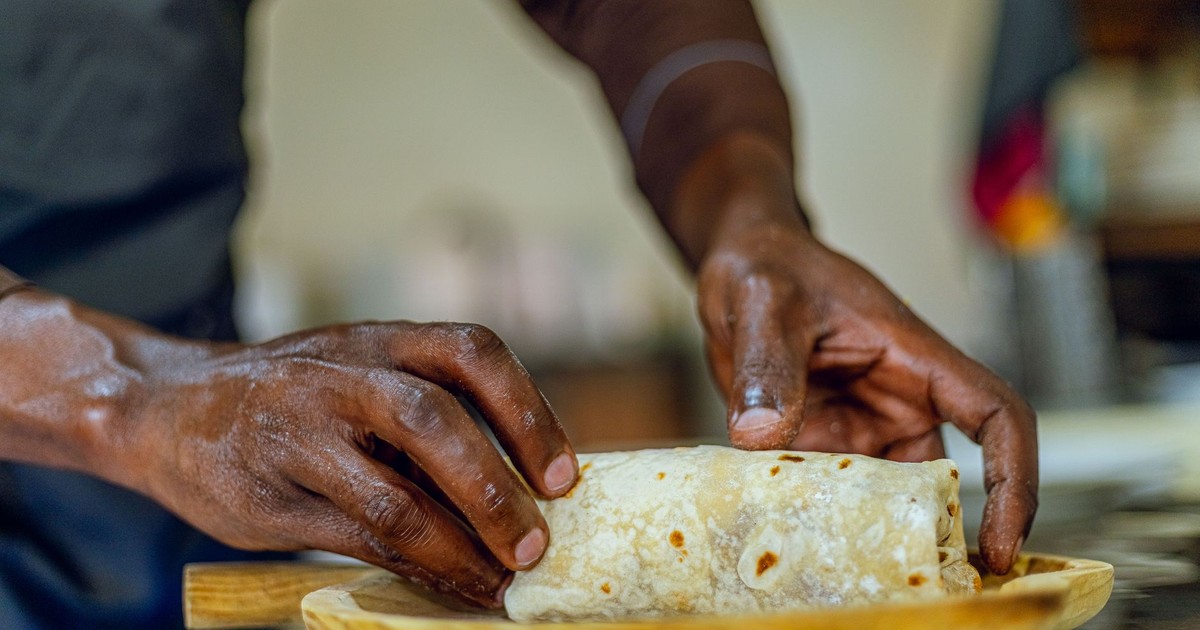 Close-up of hands wrapping a burrito on a wooden board in a kitchen setting.