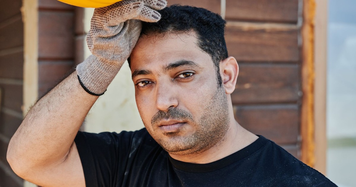 Close-up portrait of a construction worker resting, holding his hard hat. Gloved hand, thoughtful expression.