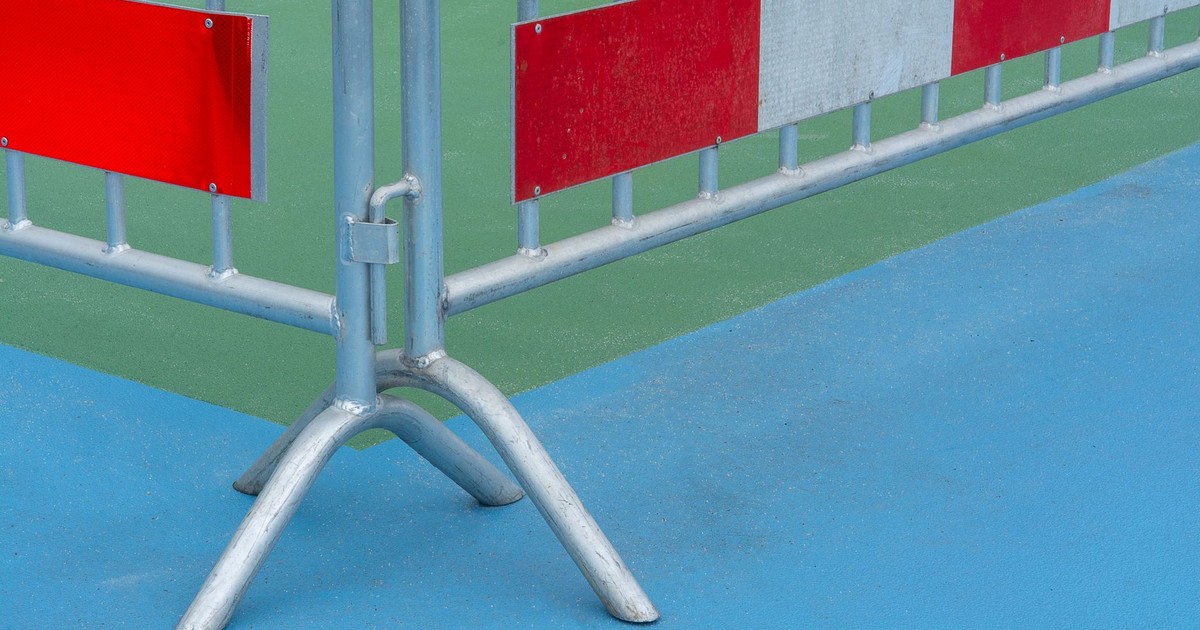 Metal barrier with red caution sign on a vibrant blue and green background outdoors.