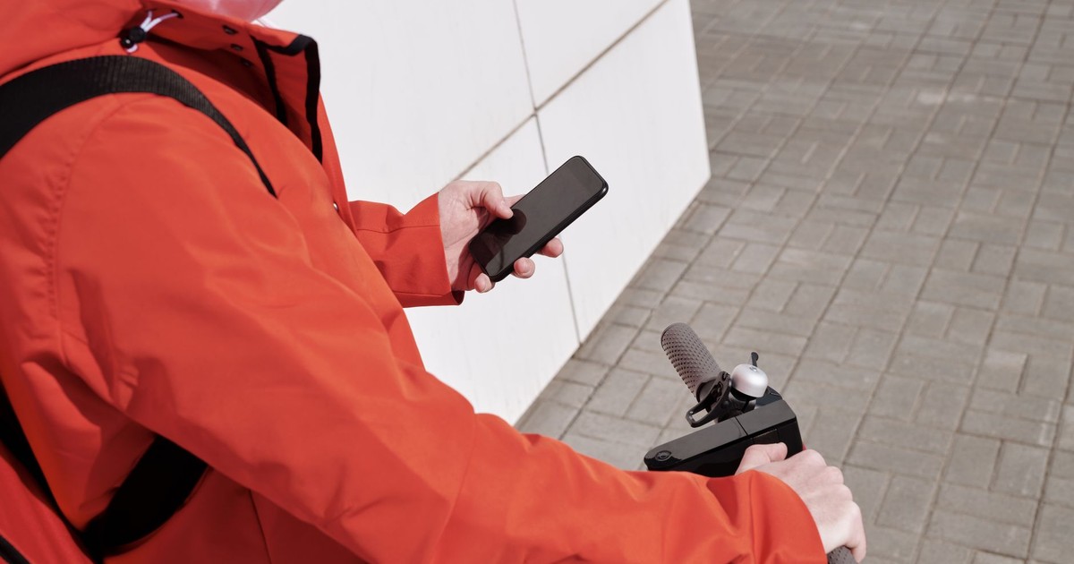Person in red jacket using smartphone while riding a scooter outdoors.
