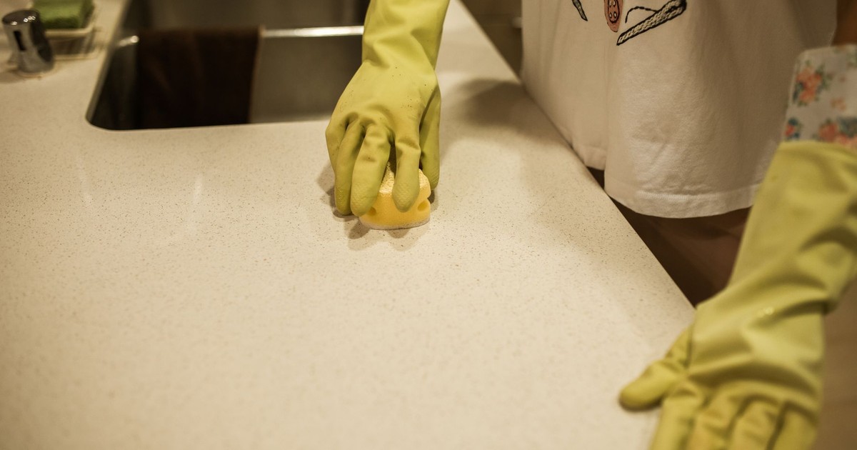 Woman using yellow rubber gloves to clean a kitchen counter with a sponge.