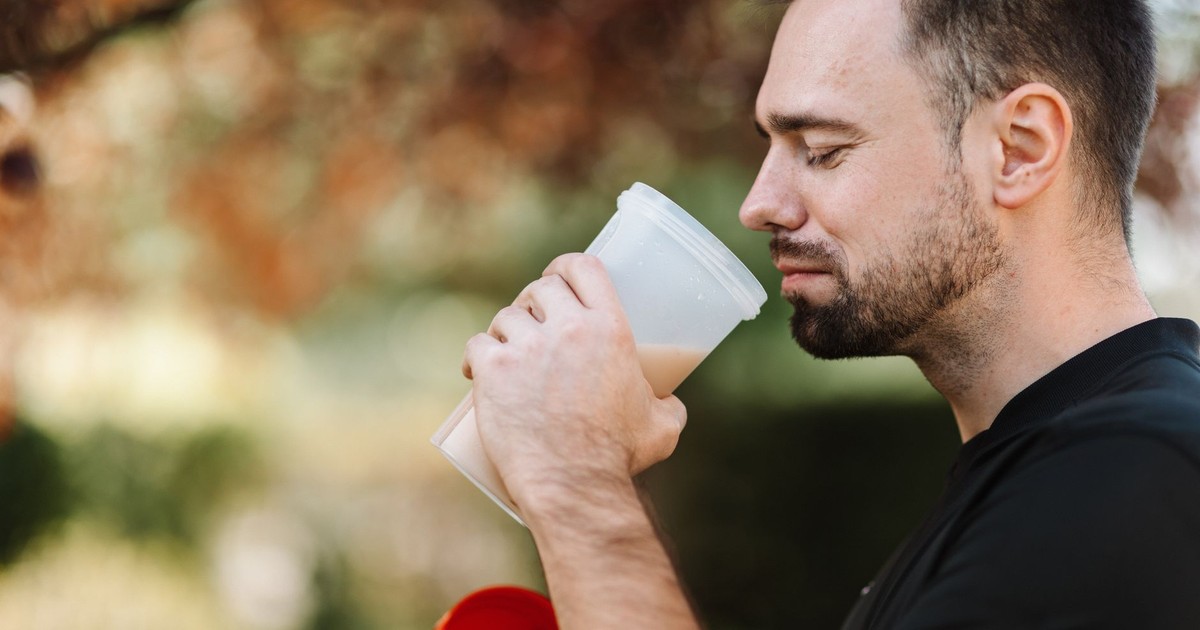 Adult man savoring a protein shake in a peaceful outdoor setting during the day.