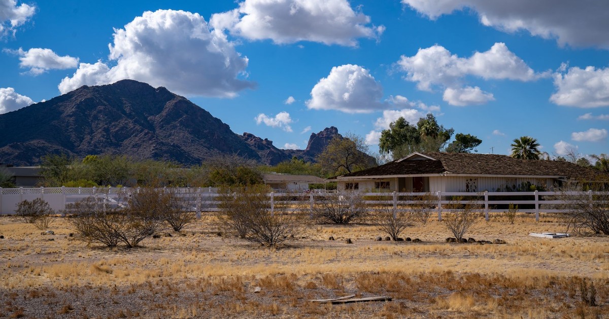 Charming rural farmhouse set against Arizona's stunning mountain scenery, under a bright blue sky.