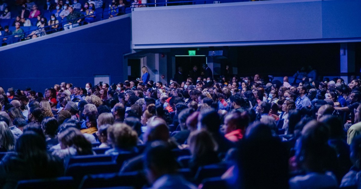 A crowded conference hall with diverse audience attentively listening to a speaker.