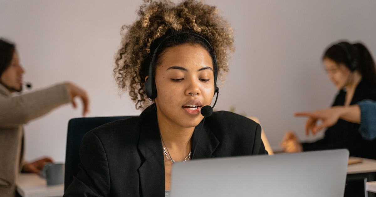 Customer support agent with headset working on laptop in office.
