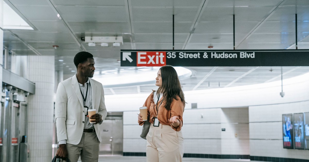 Two office workers engage in conversation at a modern subway station.