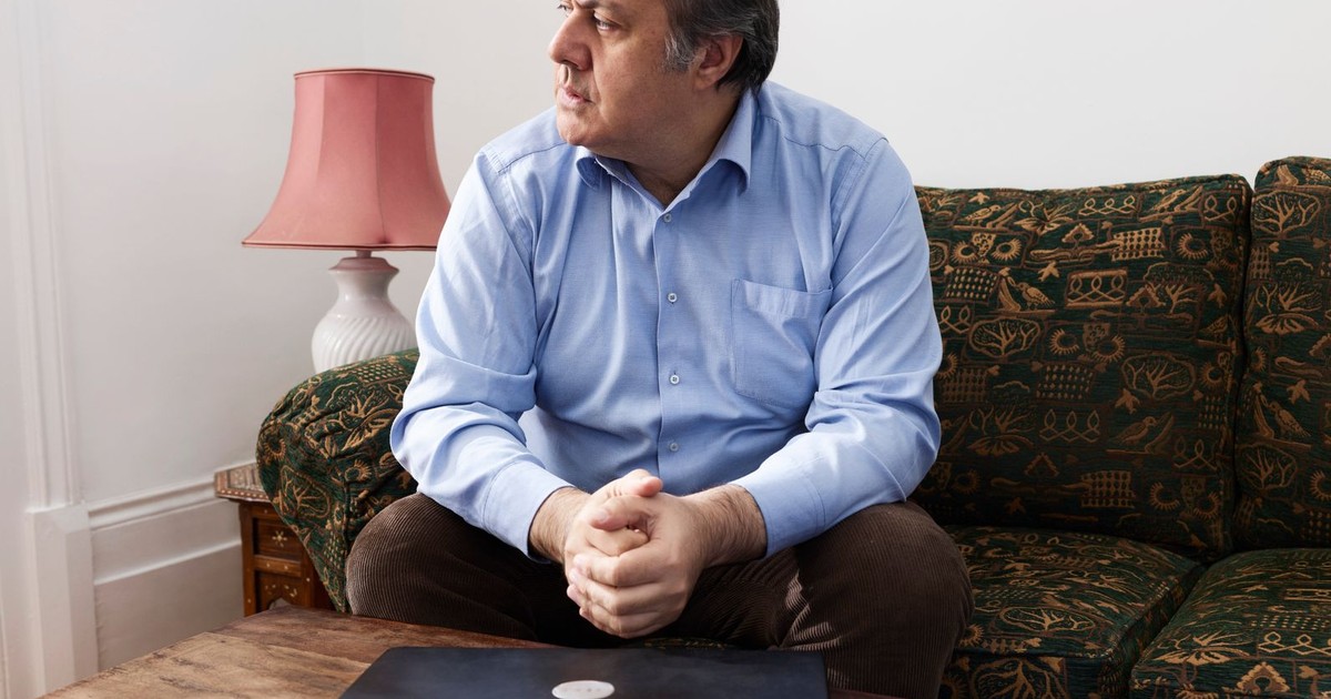 Middle-aged man sitting on a couch beside a closed laptop, depicting digital disconnection.