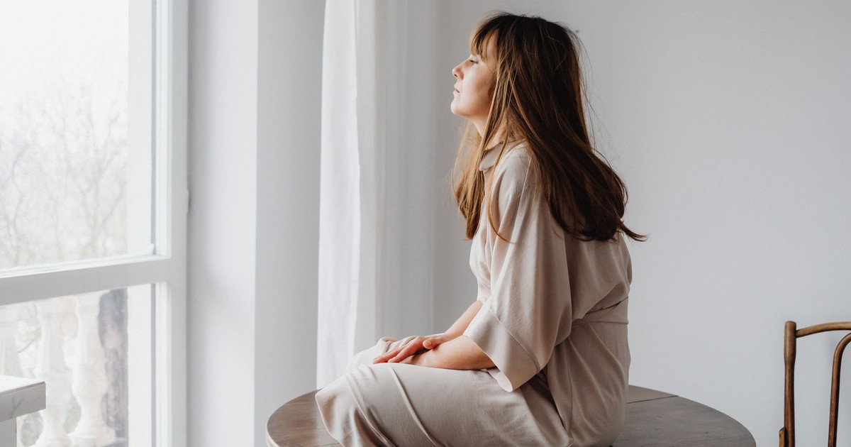 Contemplative woman sitting by a window in a minimalist white room. Perfect for themes of introspection.
