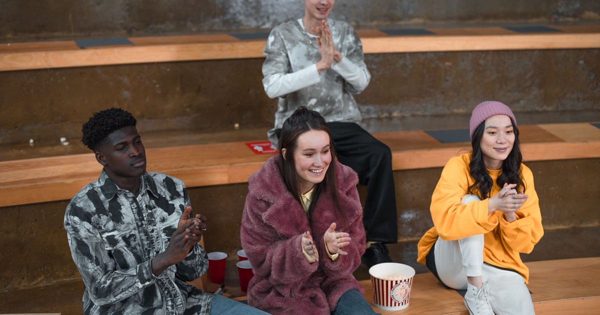A diverse group of young adults sitting in bleachers, clapping and enjoying togetherness indoors.