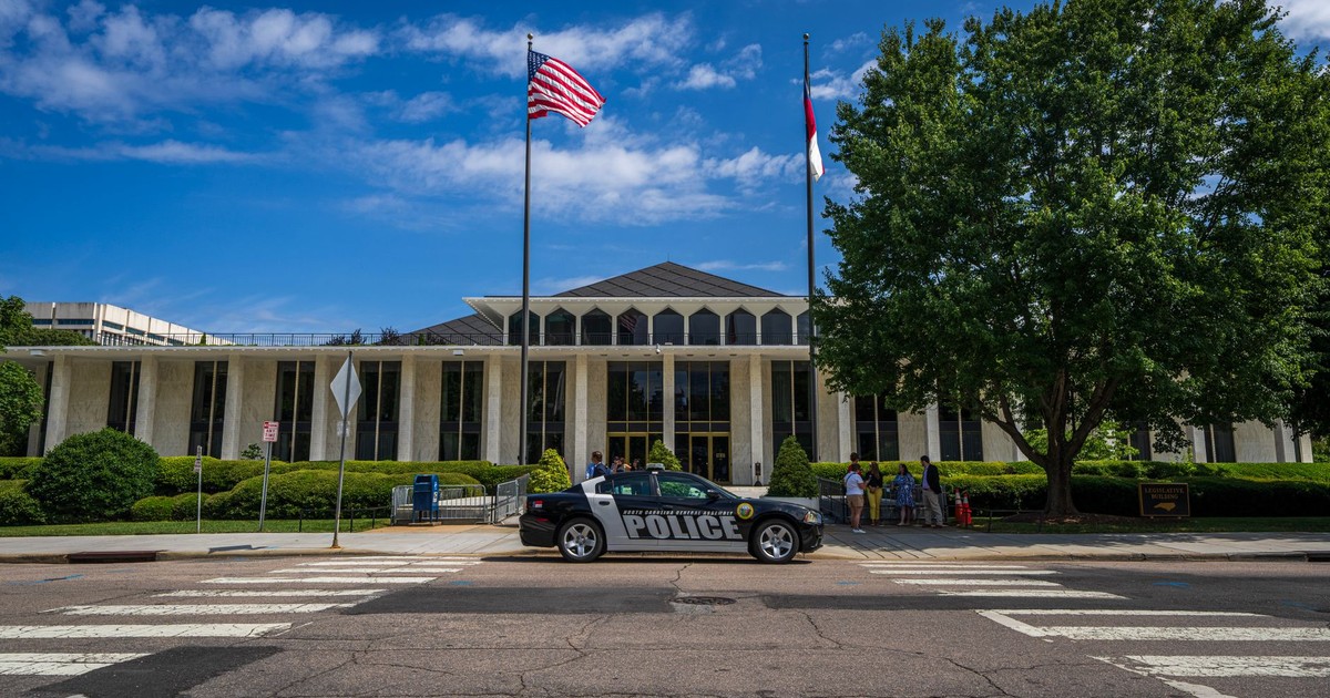 Government building facade with flags and police car in front on a sunny day.