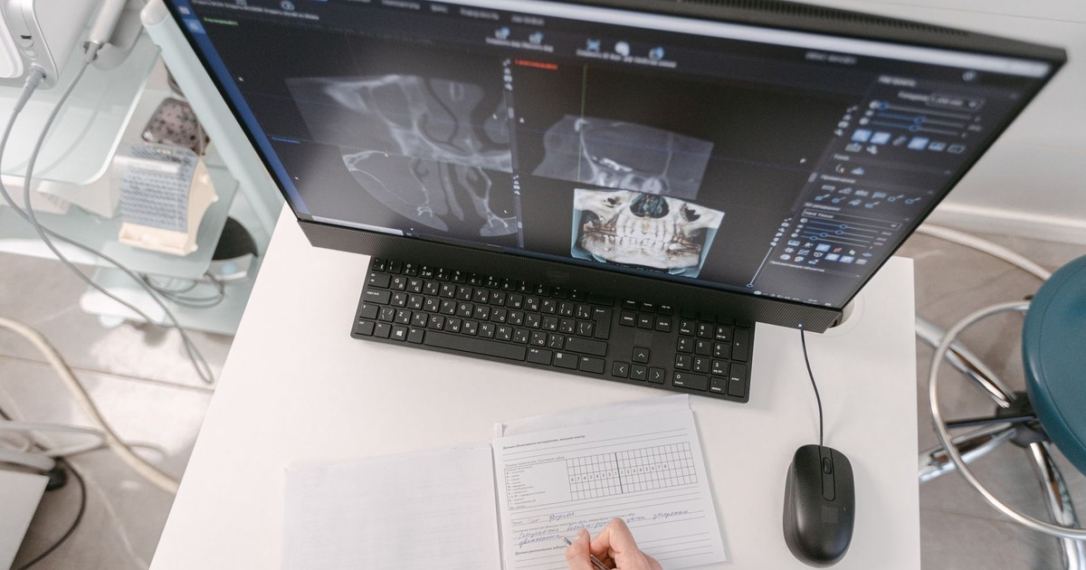 Radiologist analyzing X-ray scans on a computer monitor while taking notes. Medical documents visible.