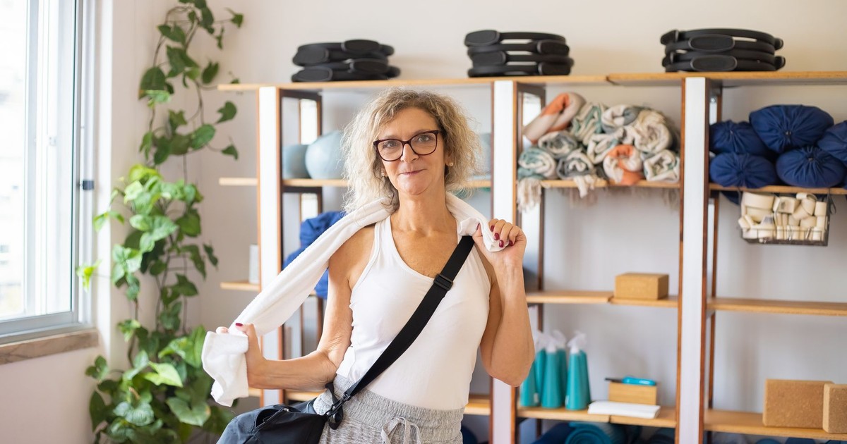 Elderly woman holding a towel in a yoga studio, surrounded by yoga equipment.
