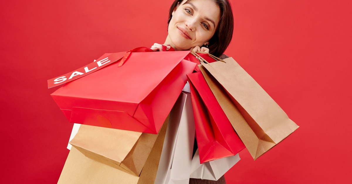 A cheerful woman holding multiple shopping bags with a sale on a red background.