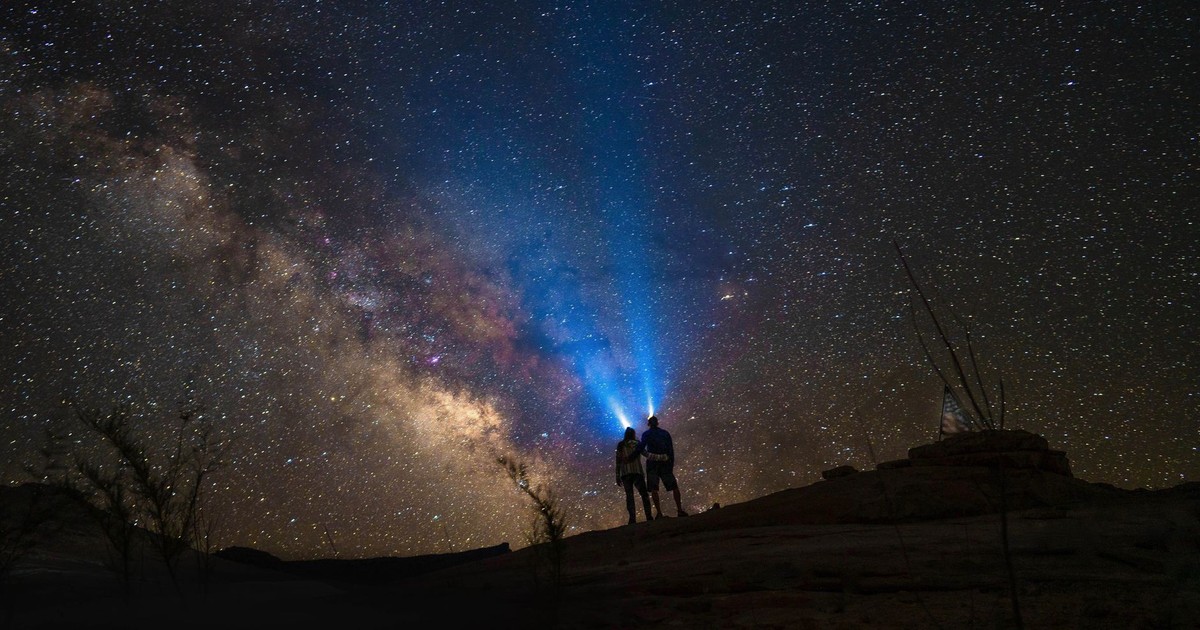A couple stargazes under the stunning Milky Way, embracing romance and nature's beauty.