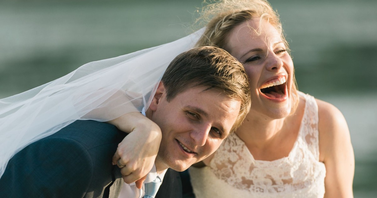 Happy bride and groom laughing together outdoors by the water.