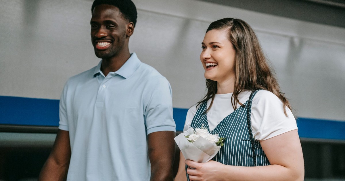 A cheerful interracial couple holding flowers, captured indoors, showcasing love and joy.