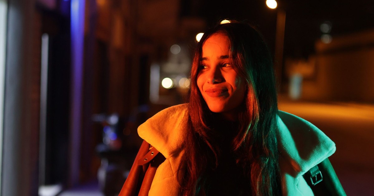 Smiling woman in a coat captured on a city street at night with vibrant lighting.