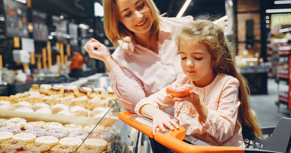 A joyful moment between mother and daughter as they shop for colorful doughnuts in a supermarket.