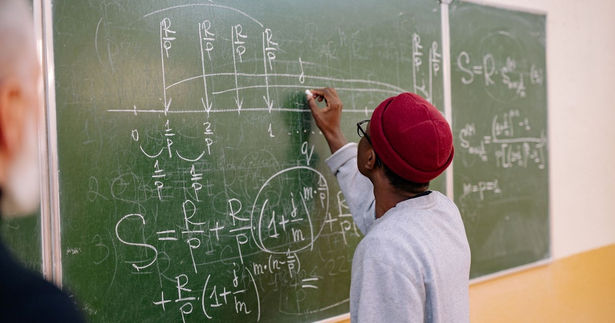 A young student writes mathematical equations on a green blackboard with precision and focus.