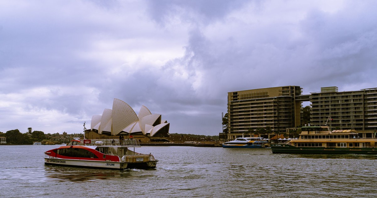Scenic view of Sydney Opera House and bustling harbor in cloudy weather, New South Wales, Australia.