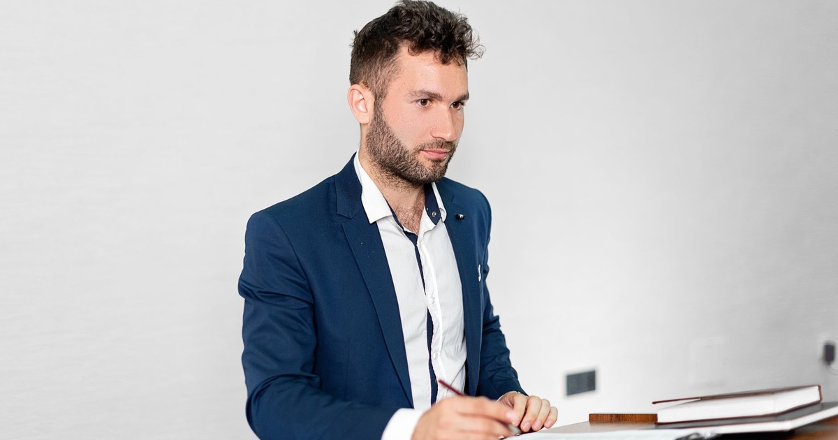 Confident businessman in a blazer presenting at a podium indoors.