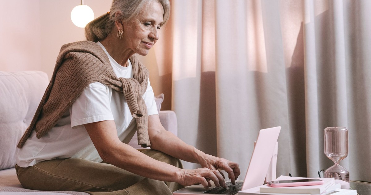 An elderly woman sits comfortably indoors using a laptop, highlighting modern technology use among seniors.
