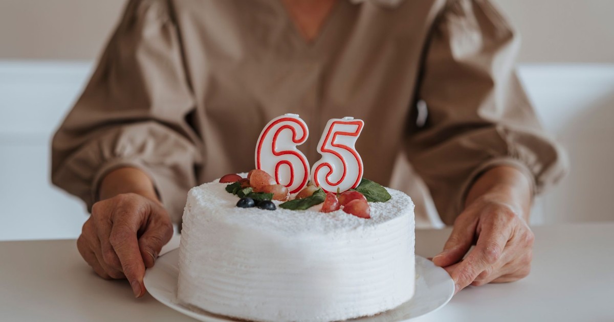 Elegant 65th birthday cake with candles and fruit garnishes.