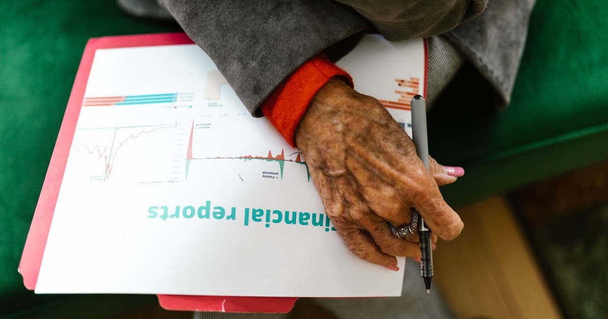 Close-up of an elderly woman holding a pen with a financial report.