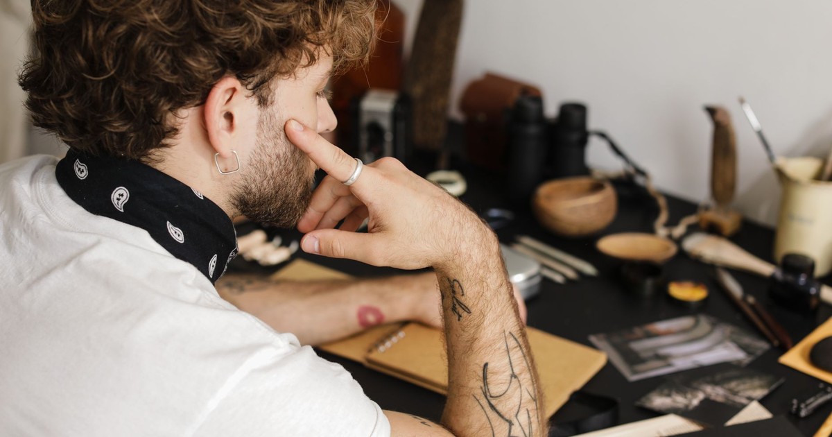 A thoughtful man with tattoos considers his artistic work in a creative workspace.