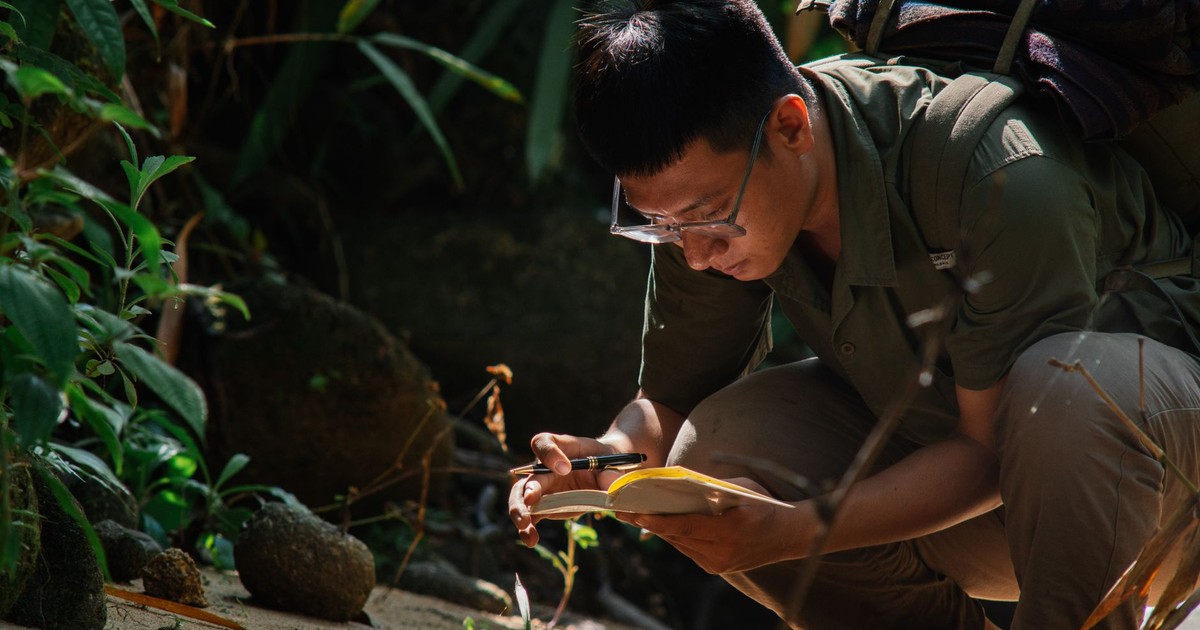 Man crouching outdoors, writing in a notebook surrounded by lush greenery, showcasing a peaceful, contemplative moment.